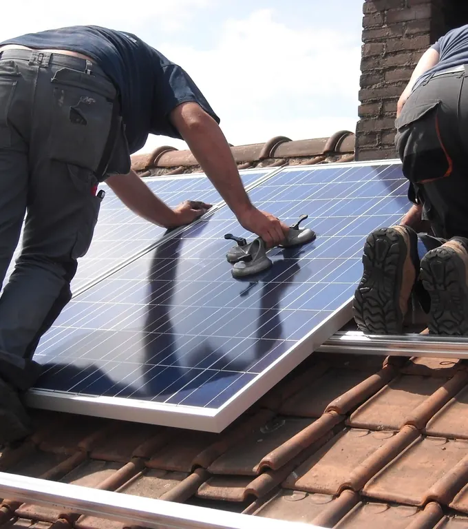Installateurs à genoux sur un toit en tuiles plaçant un module solaire
