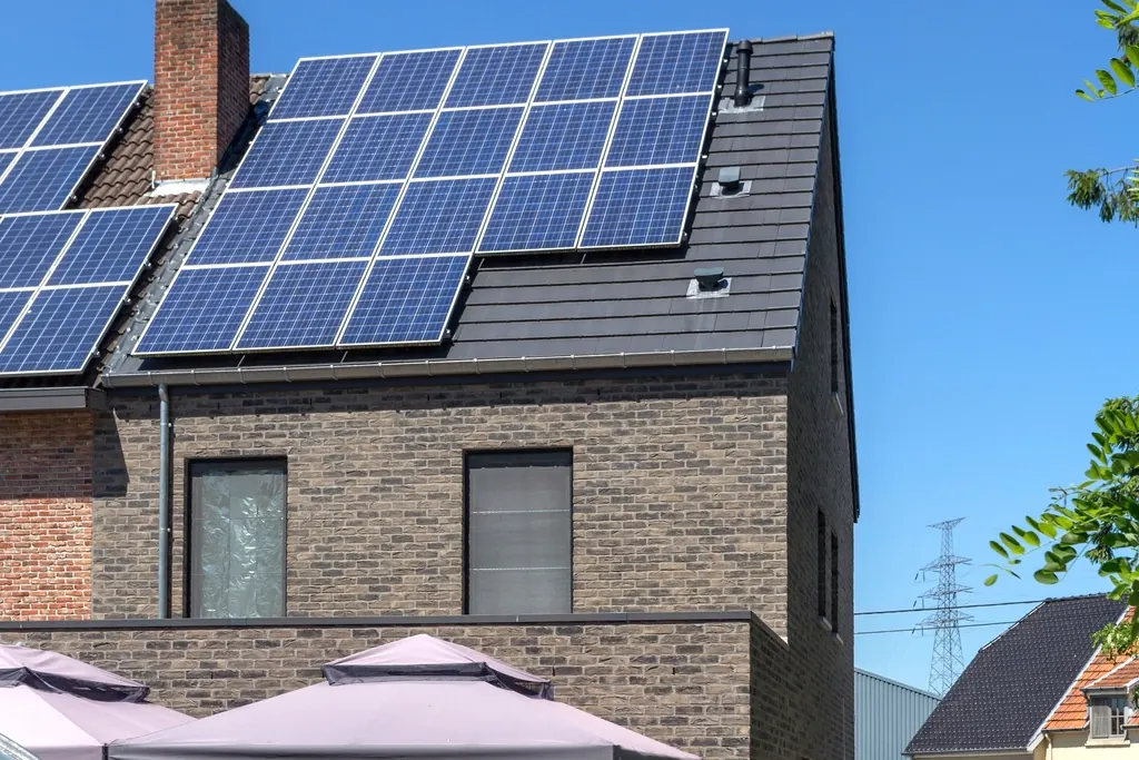 Pignon de maison en brique avec panneaux solaires sur un toit sombre sous un ciel bleu